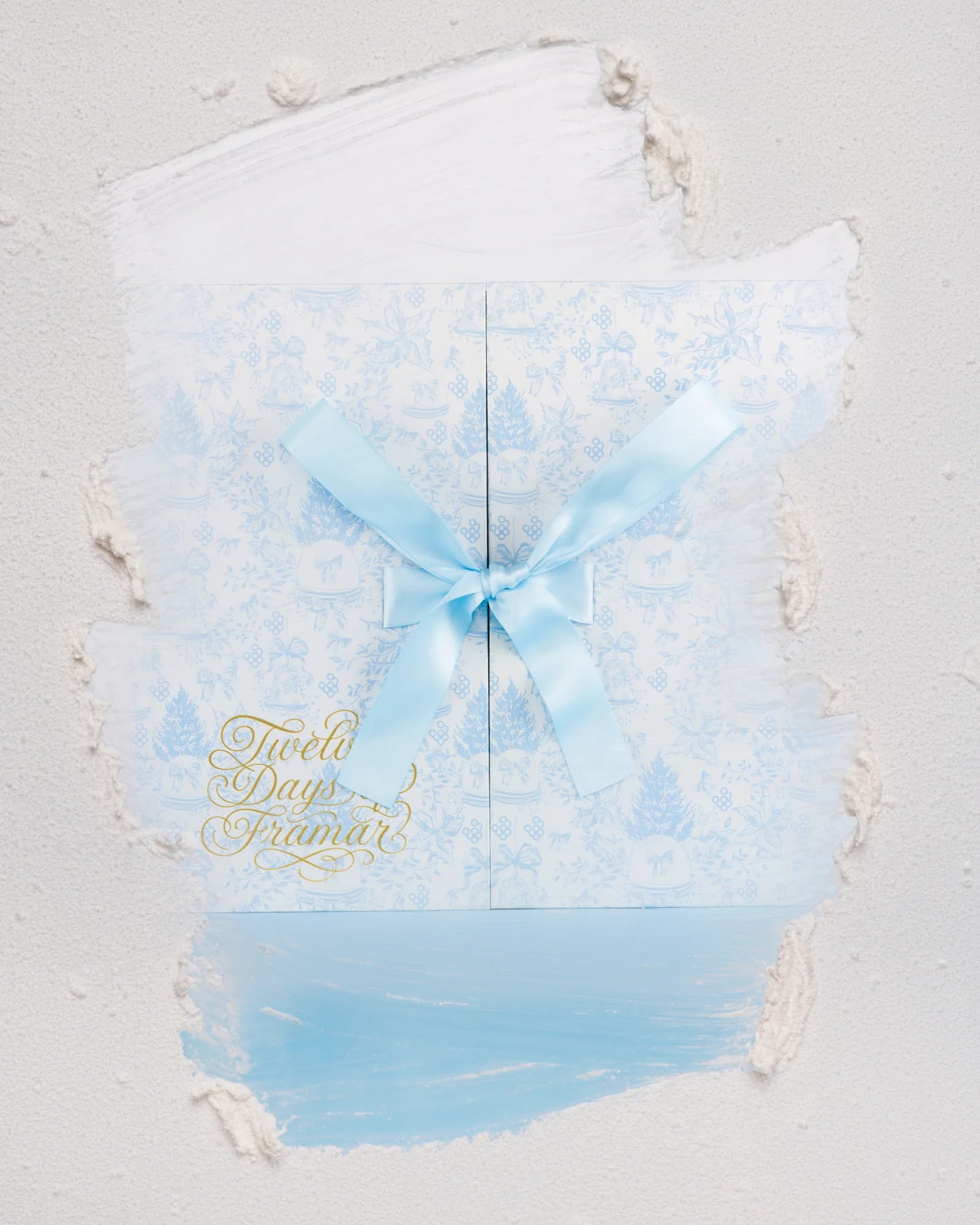 Twelve Days of Framar 2026 calendar wrapped in a blue ribbon and surrounded by snow